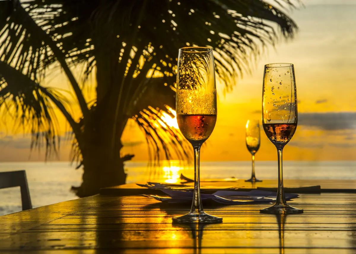 sekt_prosecco_champagner_sonnenuntergang_palmen_meer_zwei_glaeser_holztisch